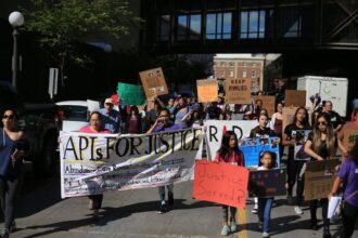 An image of 70 community members gather together, there is a banner at the front that says 