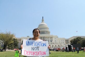 Person holds up anti-deportation sign in front of Capitol building.