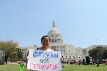 Person holds up anti-deportation sign in front of Capitol building.