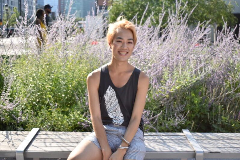 Person wears black sleeveless shirt and striped shorts sits in front of purple flowers