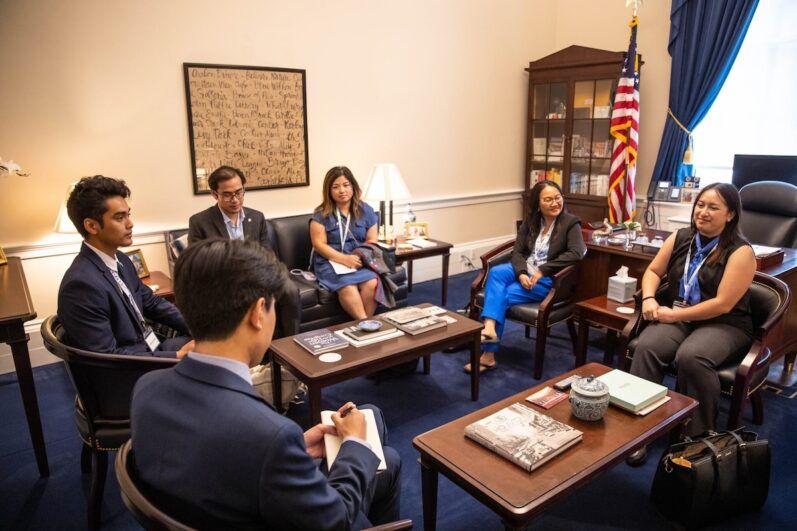 A group of individuals sit in a circle around two coffee tables in an office.