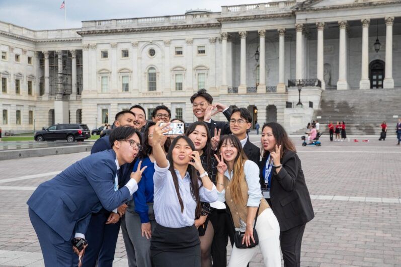 People take a group selfie in front of the Capitol building.