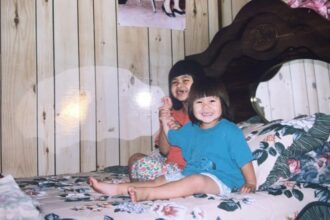 Nary as a small child sitting on a bed.