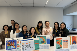 A group of people stand behind a conference table containing art prints.