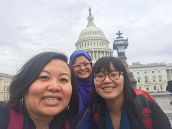 Three people pose together with the Capitol building behind them.