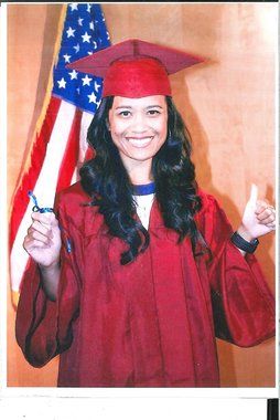 A woman in a red cap and gown smiling.