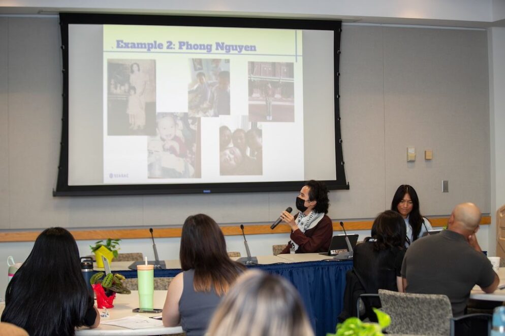 An individual holds a microphone while presenting a Powerpoint with a collage of images and 