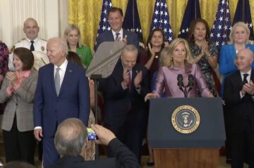 A group of individuals surround President Biden in applause.