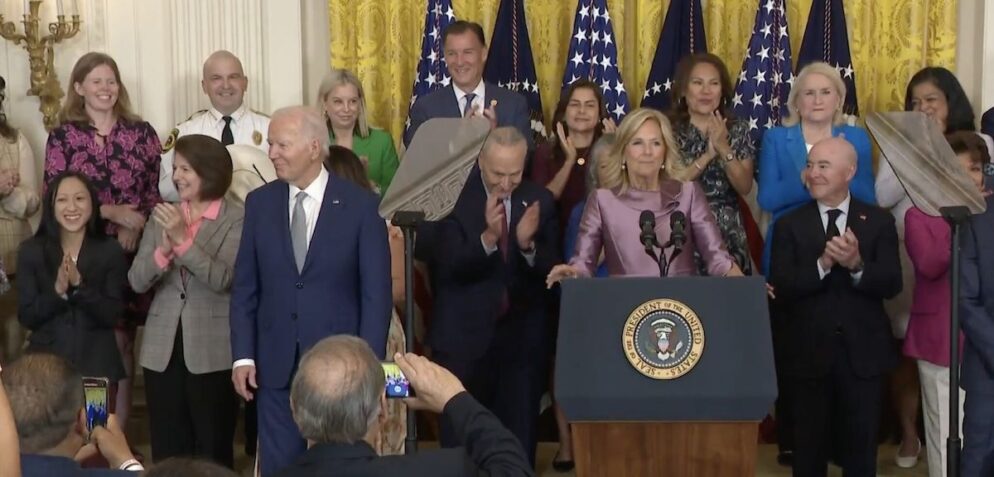 A group of individuals surround President Biden in applause.