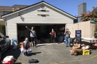 A group of people wearing masks in front of an open garage,