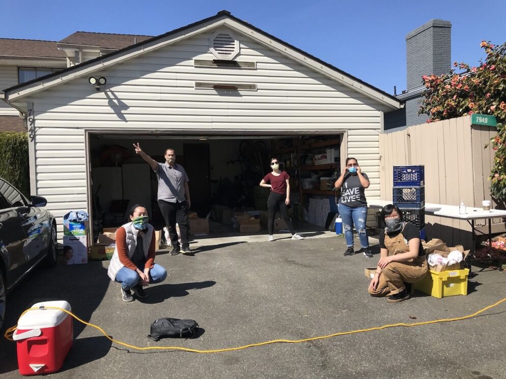 A group of people wearing masks in front of an open garage,