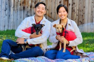 Two people smiling, each holding dogs