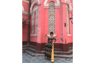 Person poses in front of a pink building.