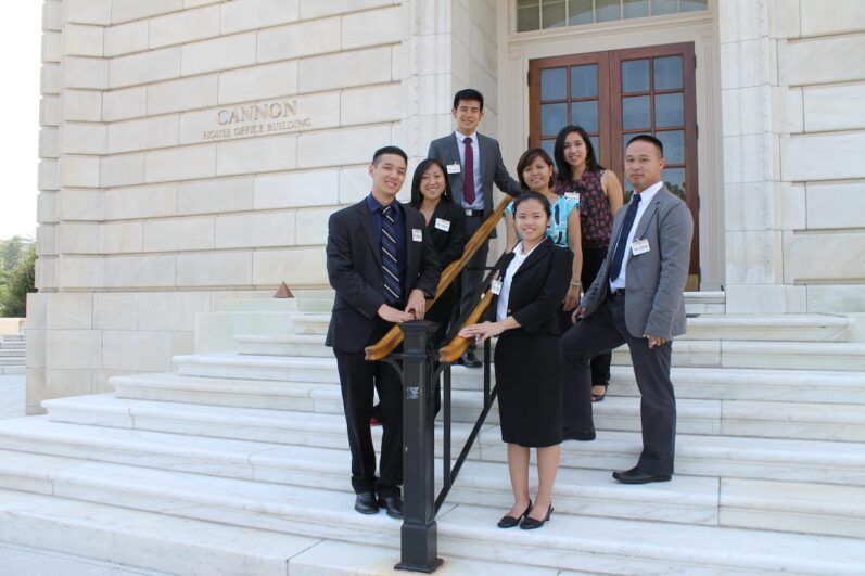 A group of seven individuals in smart dress pose in front of a building.