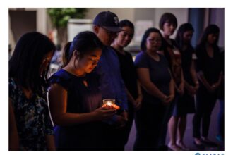 People gathering in a dark room with a woman holding a lit candle.