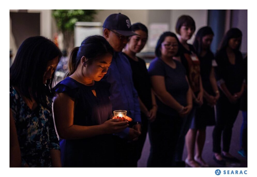 People gathering in a dark room with a woman holding a lit candle.