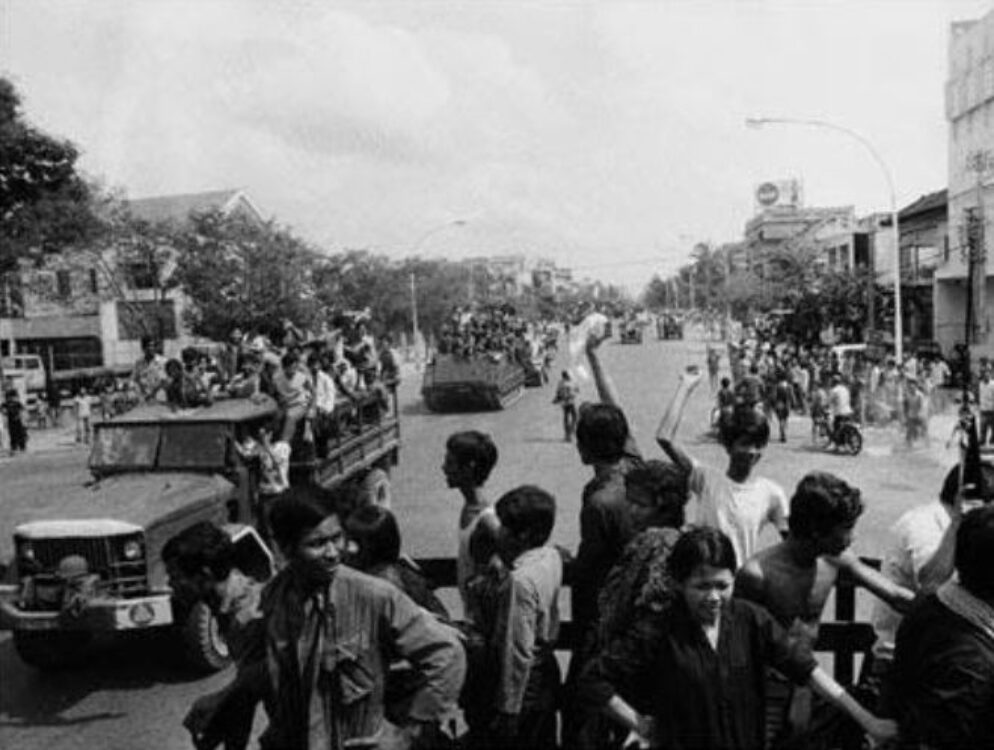 Cambodians raising their fists on moving vehicles.