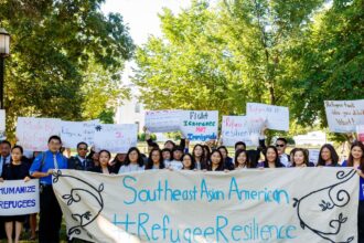 People hold up a stating Southeast Asian Refugee Resilience banner