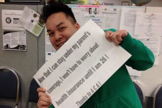 Person in green shirt holds up a sign thanking ACA for giving health coverage