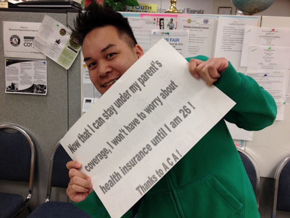 Person in green shirt holds up a sign thanking ACA for giving health coverage