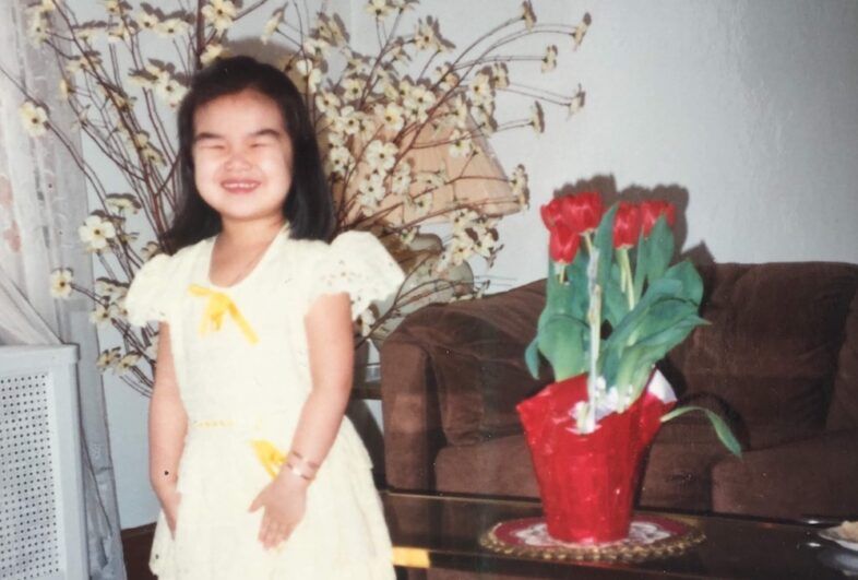 A child wearing a yellow dress smiles proudly in a living room