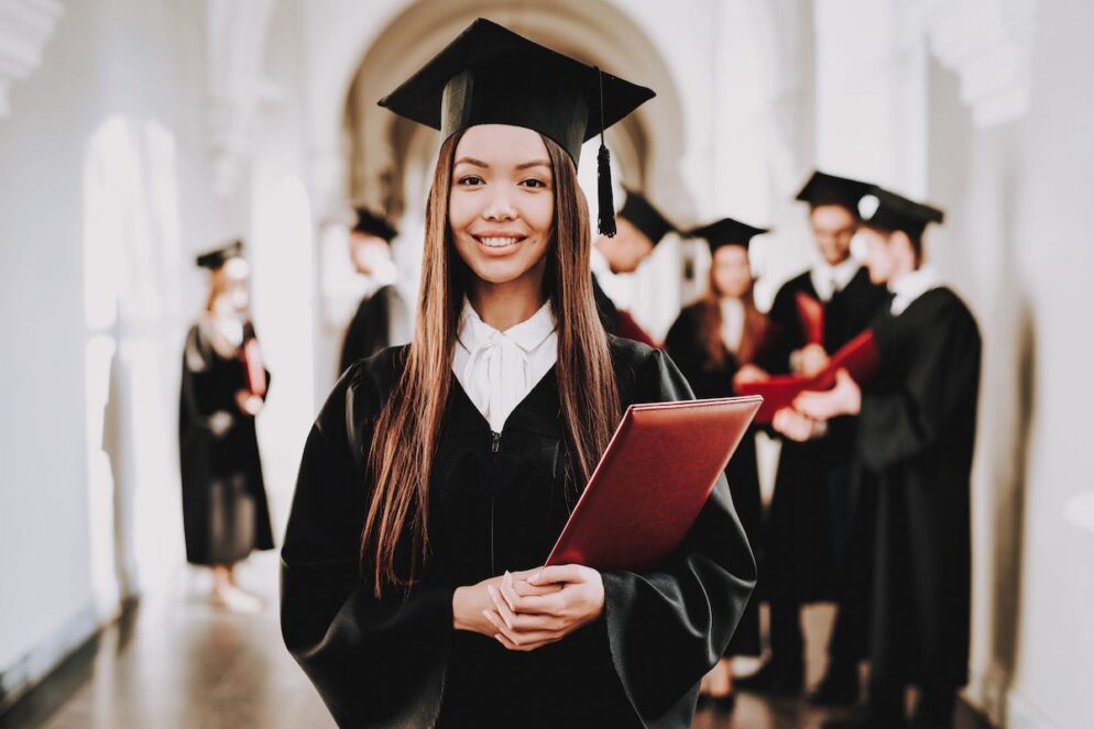 Person wears graduation robes, smiling