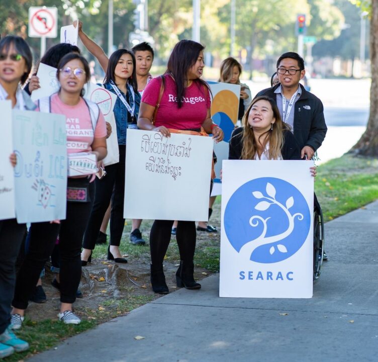 People hold signs while near a sidewalk, one person holds a SEARAC sign