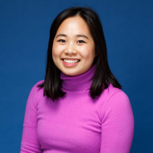 A person wearing a pink turtle neck and smiling