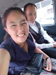 A selfie of Moua and Dokmai smiling in the back seat of a car.