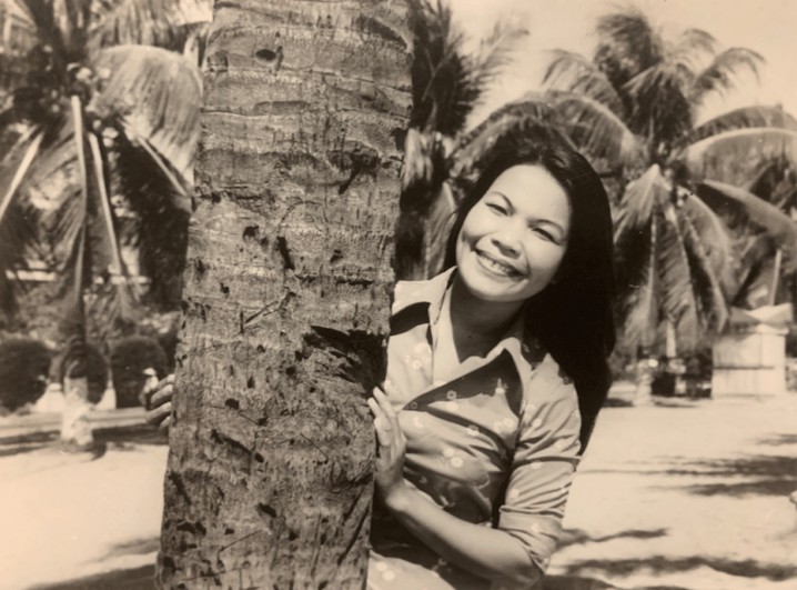 An's mother smiling behind a tree.