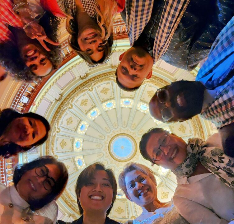 A group of people form a circle and look down at a camera