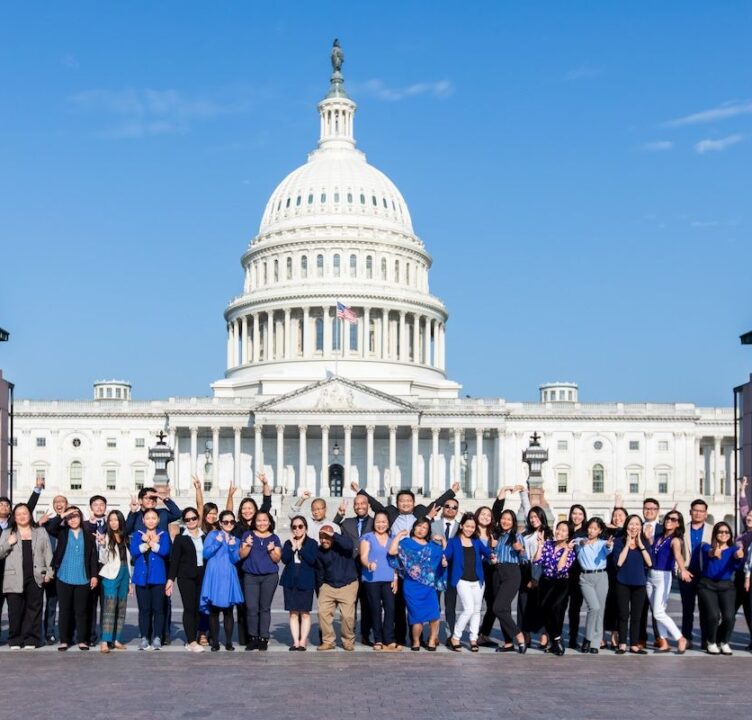 Dozens of people, wearing blue formal attier, stand in front of the Capitol building