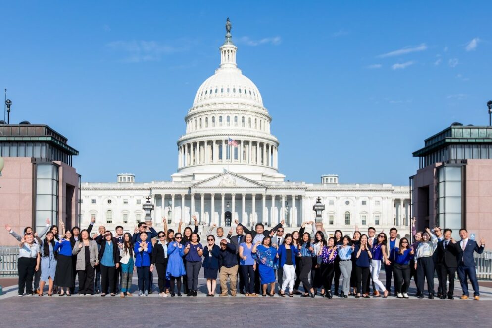 Dozens of people, wearing blue formal attier, stand in front of the Capitol building