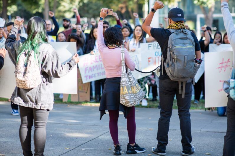 three people face a crowd, hands raised