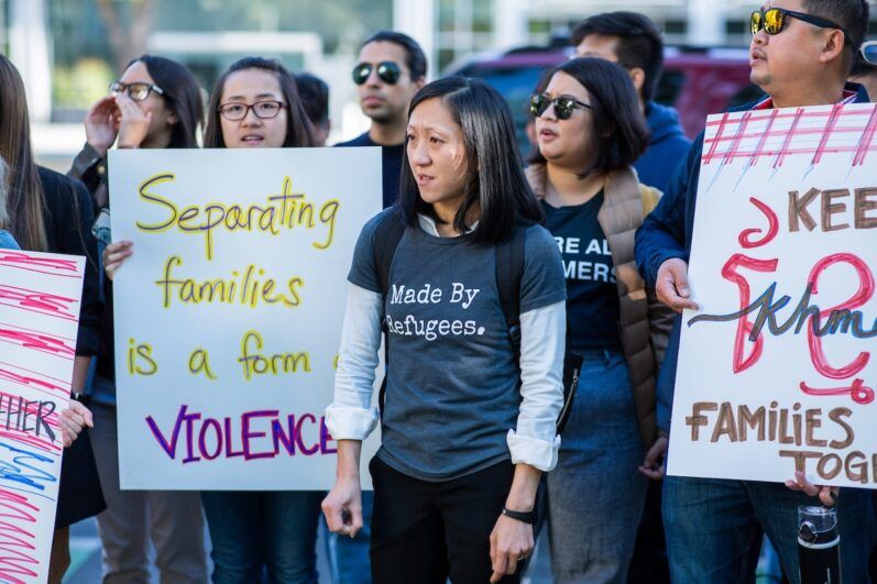 Quyen wears a Made by Refugee shirt at a rally, people behind her hold signs