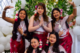 Six people wear traditional attire adorned with flowers