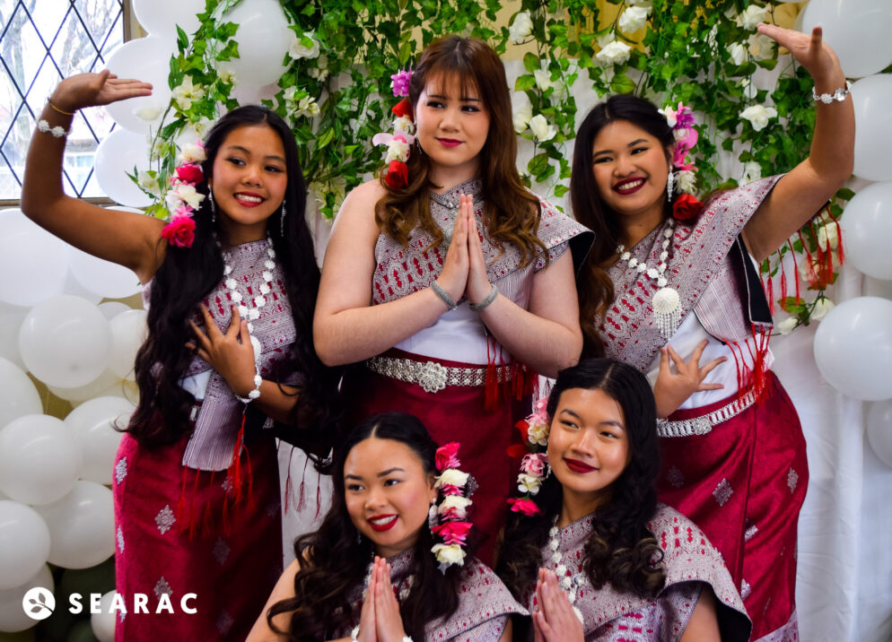 Six people wear traditional attire adorned with flowers