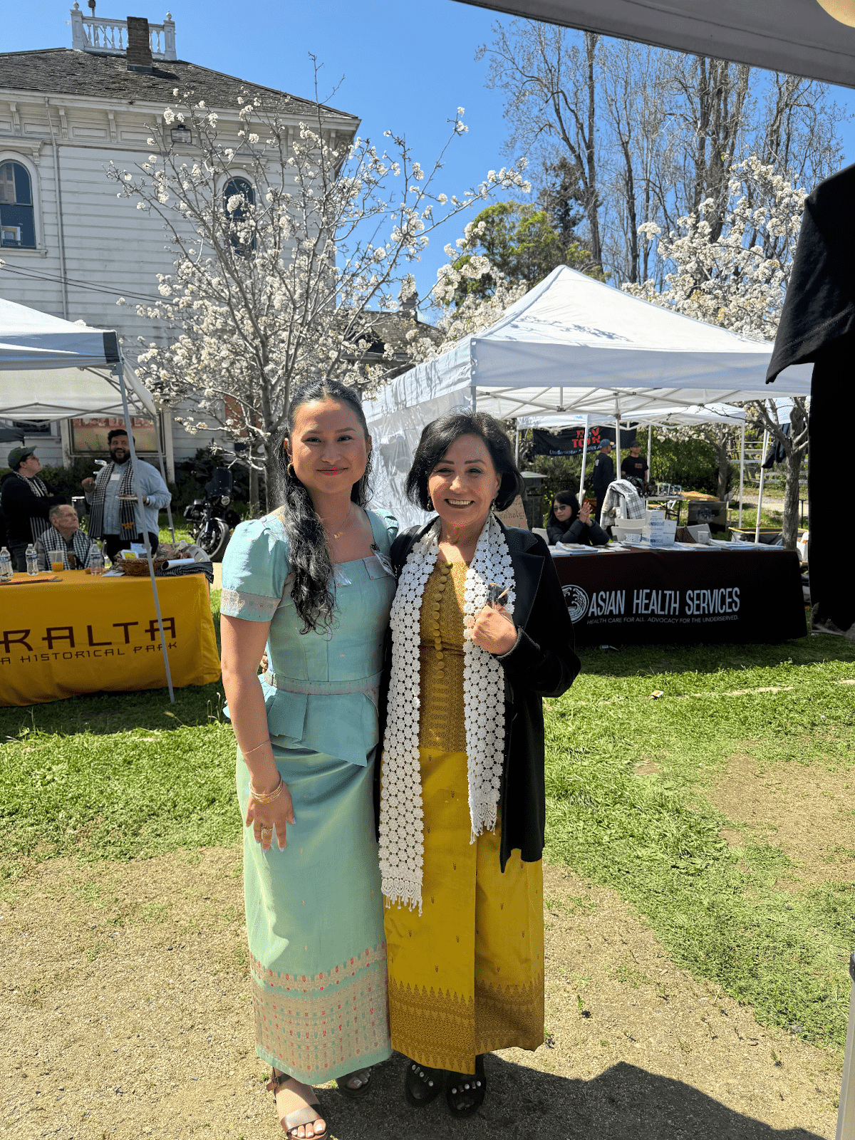 Two people smiling together outside. They are wearing traditional Cambodian clothing. 