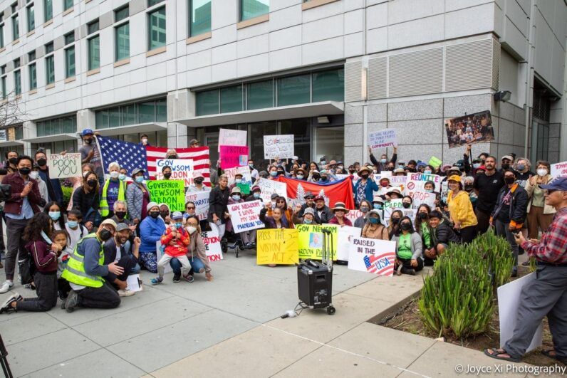 A community rallying together for immigration justice. There are signs and flags. 