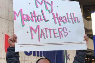 A man smiling while holding up a mental health sign.