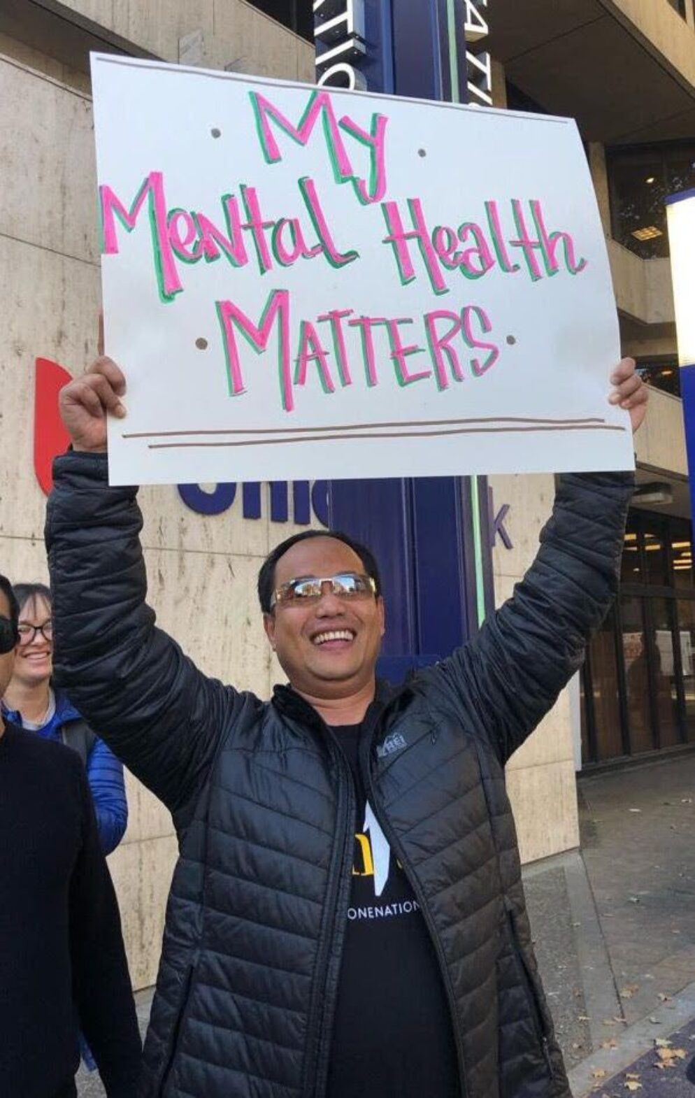 A man smiling while holding up a mental health sign.