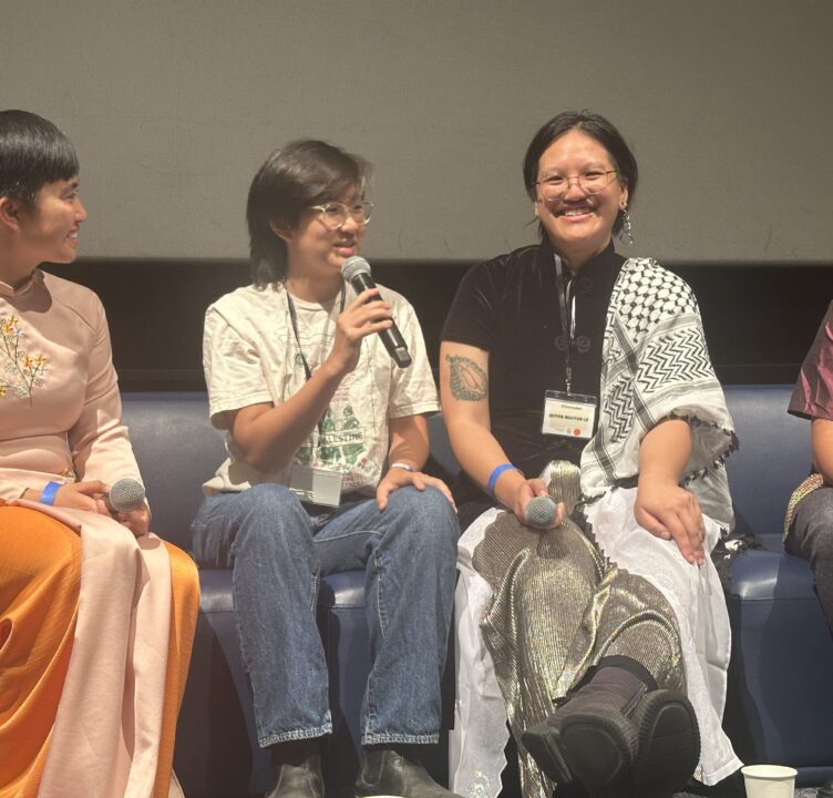 A panel of four individuals sit on a stage, with one person speaking into a microphone