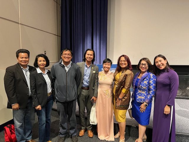 Eight people pose side by side, some in formal cultural attire