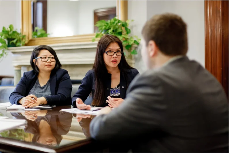 three individuals are seated at a table, in discussion, with plants in the background