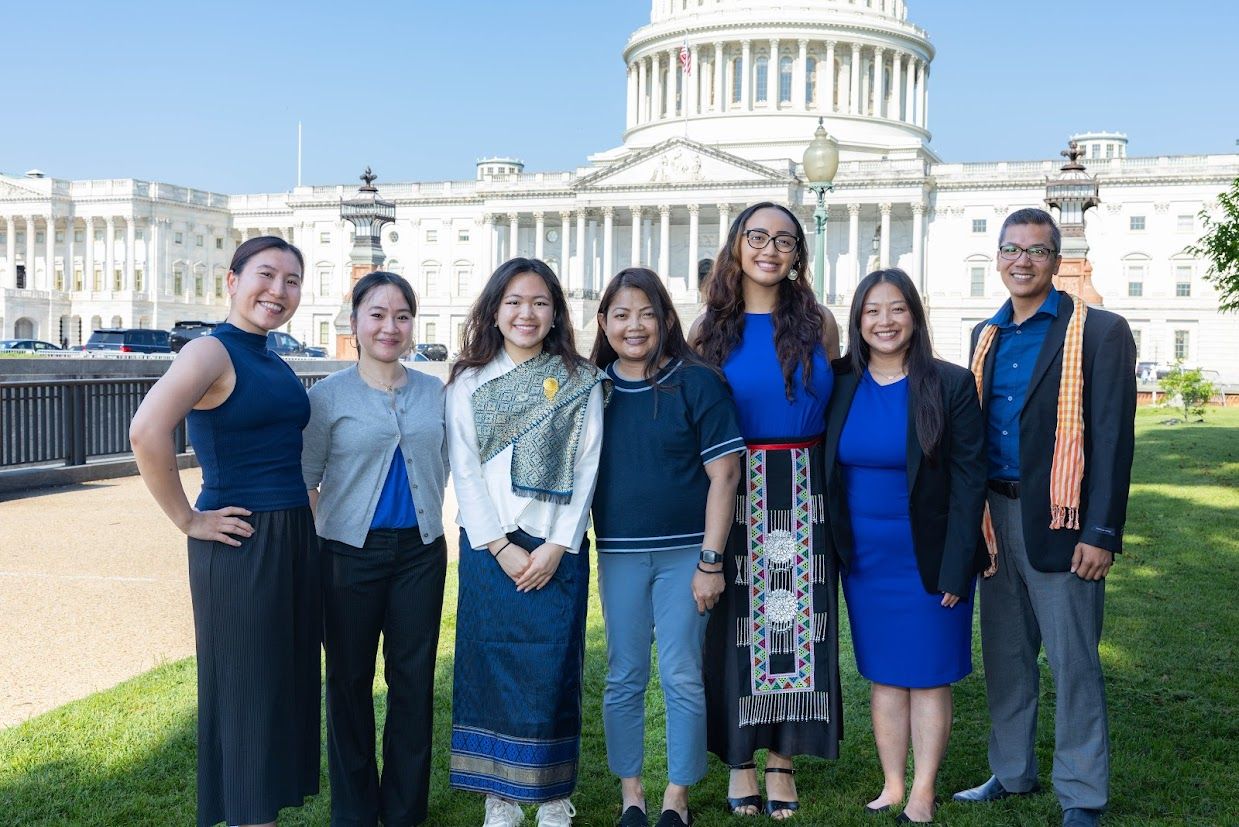 7 individuals dressed in shades of blue in business attire pose in front of the Capitol Building