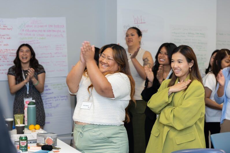 a room filled with people clapping their hands and smiling