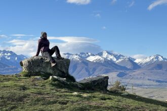 Person sits on a rock with mountains in the background