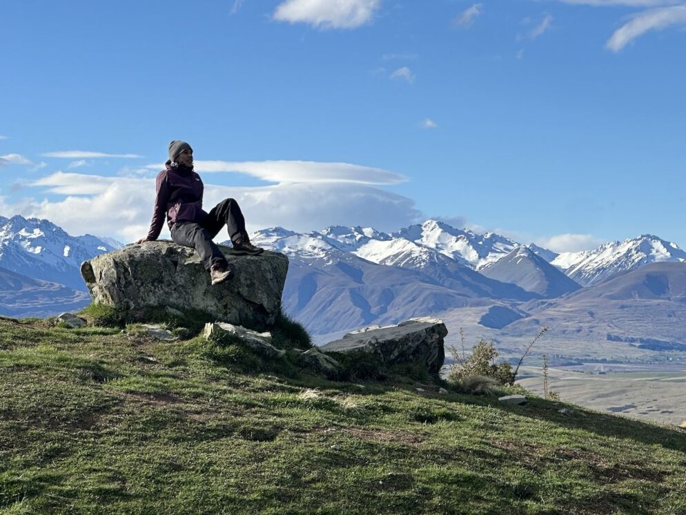 Person sits on a rock with mountains in the background