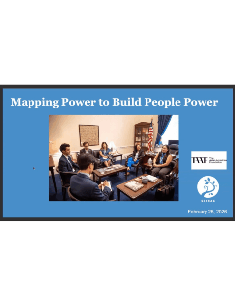 People in business attire sit around two tables inside an office